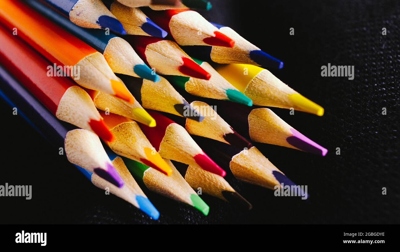 Abstract background for creativity. Lots of colored pencils on a dark background. Sharp tips of wooden pencils. Stock Photo