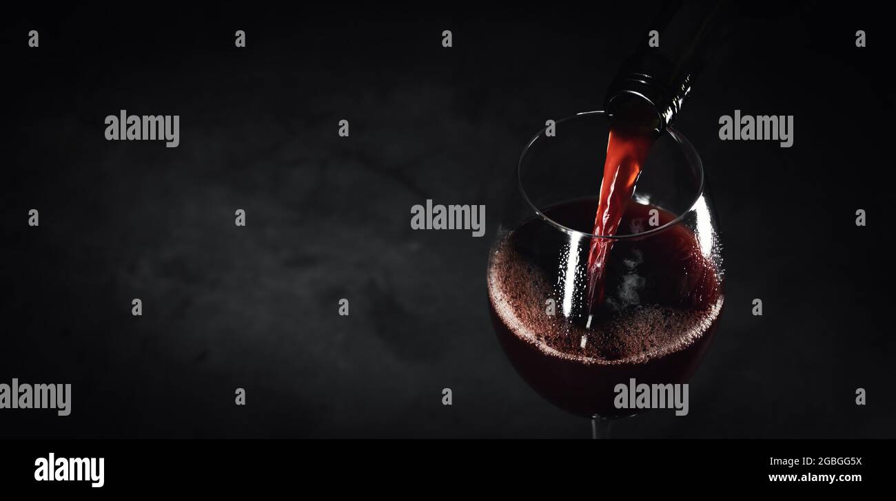 red wine pouring into a glass from bottle on a black background. banner copy space Stock Photo