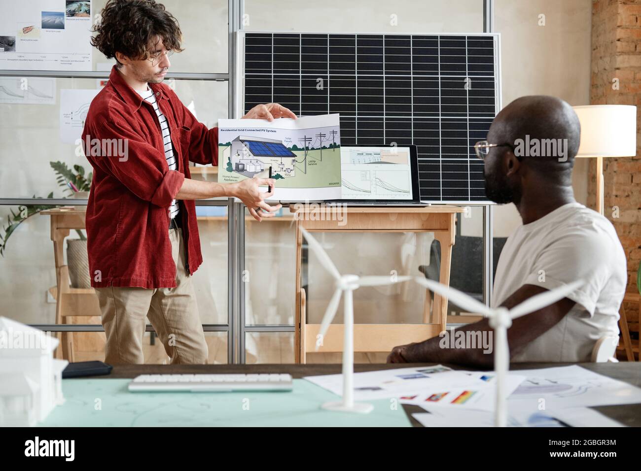 Young construction designer presenting project of modern building to business partners at meeting Stock Photo