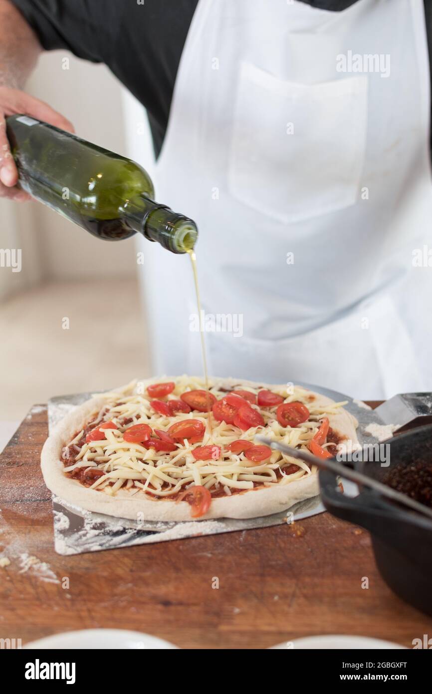 Closeup shot of male cook hand adding olive oil on a pizza, making