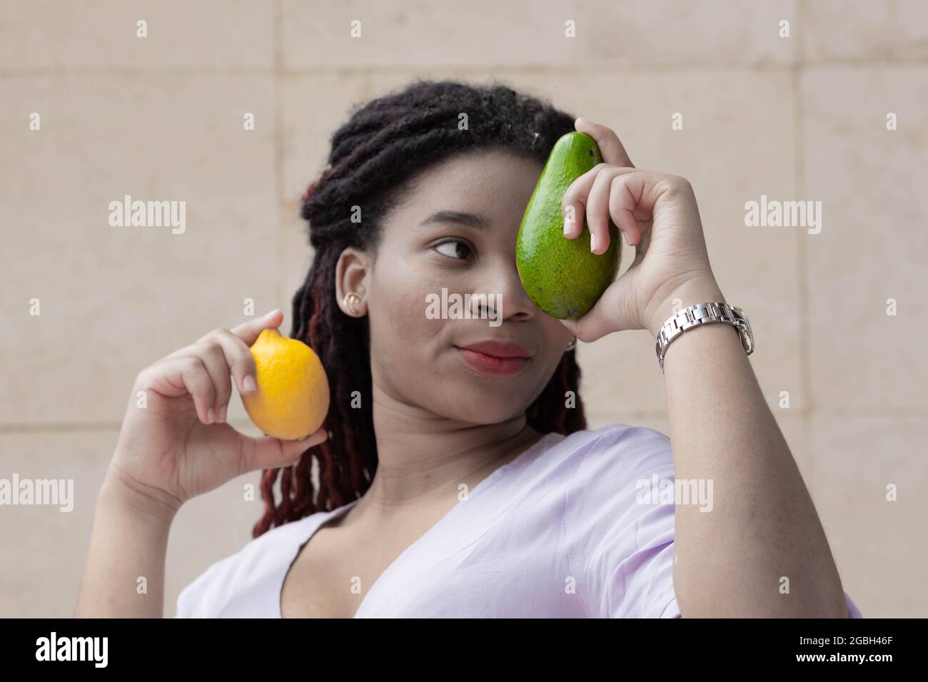 Afro woman with avocado and lemon in her hands. Avocado on the background of one woman's eye. Fruit advertising to promote vitamins. Color graded Stock Photo