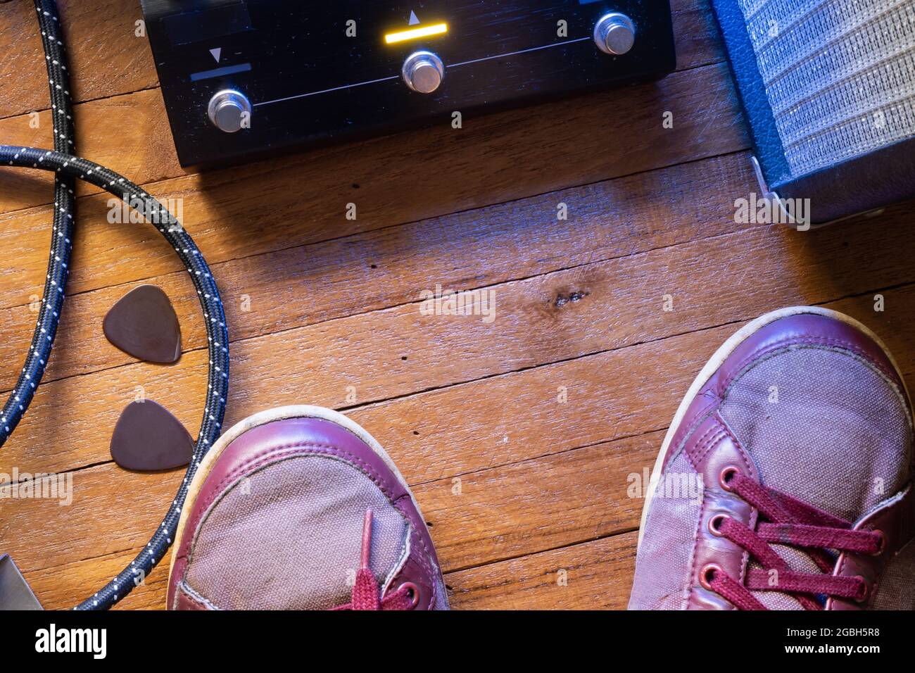 Guitarist's point of view on the stage floor. Guitar pedal, cable, guitar pick, amplifier and shoes on wooden floor. Stock Photo