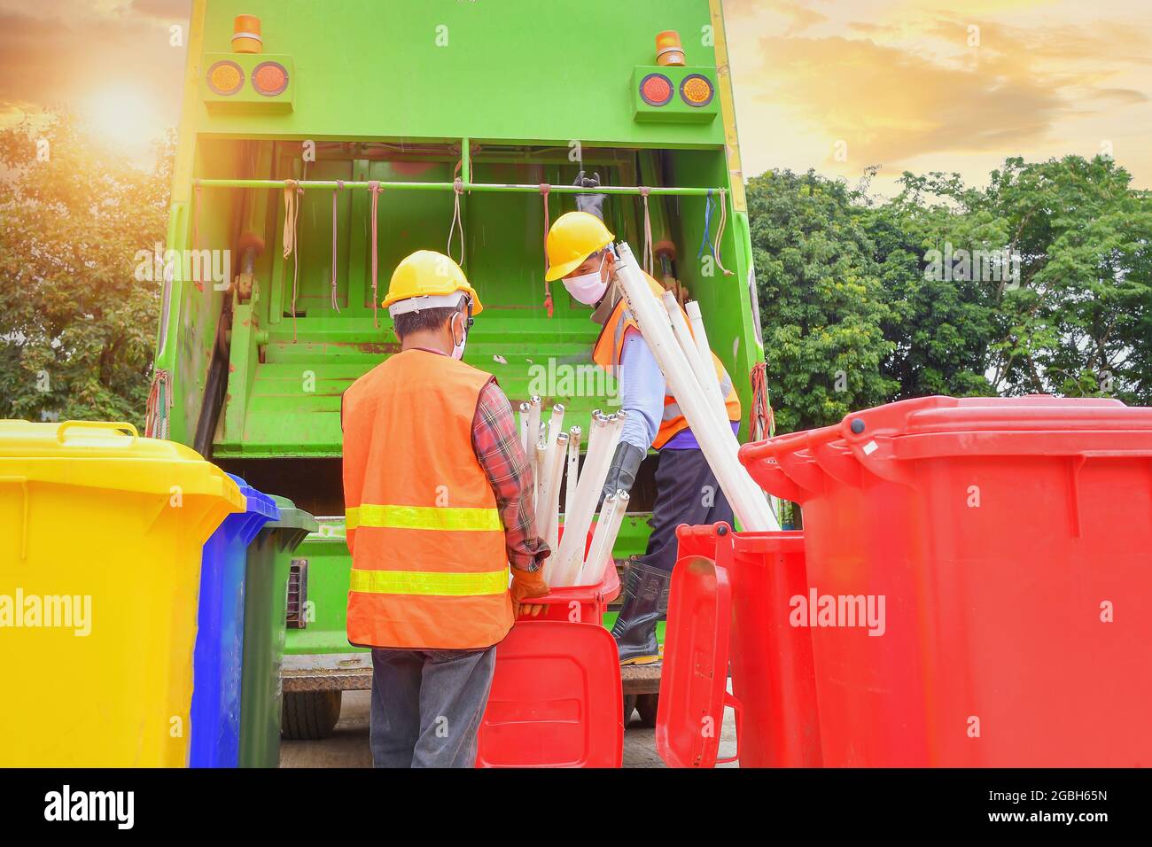 Two dustmen standing by a dustbin lorry emptying wheelie bins, Thailand Stock Photo