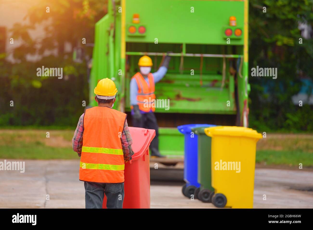 Two dustmen standing by a dustbin lorry emptying wheelie bins, Thailand Stock Photo