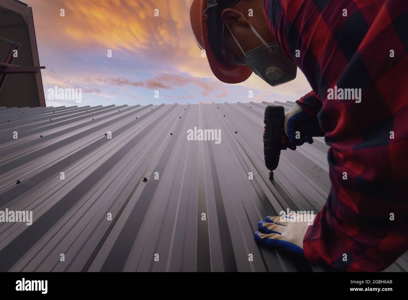 Construction worker installing metal sheets on a roof, Thailand Stock Photo