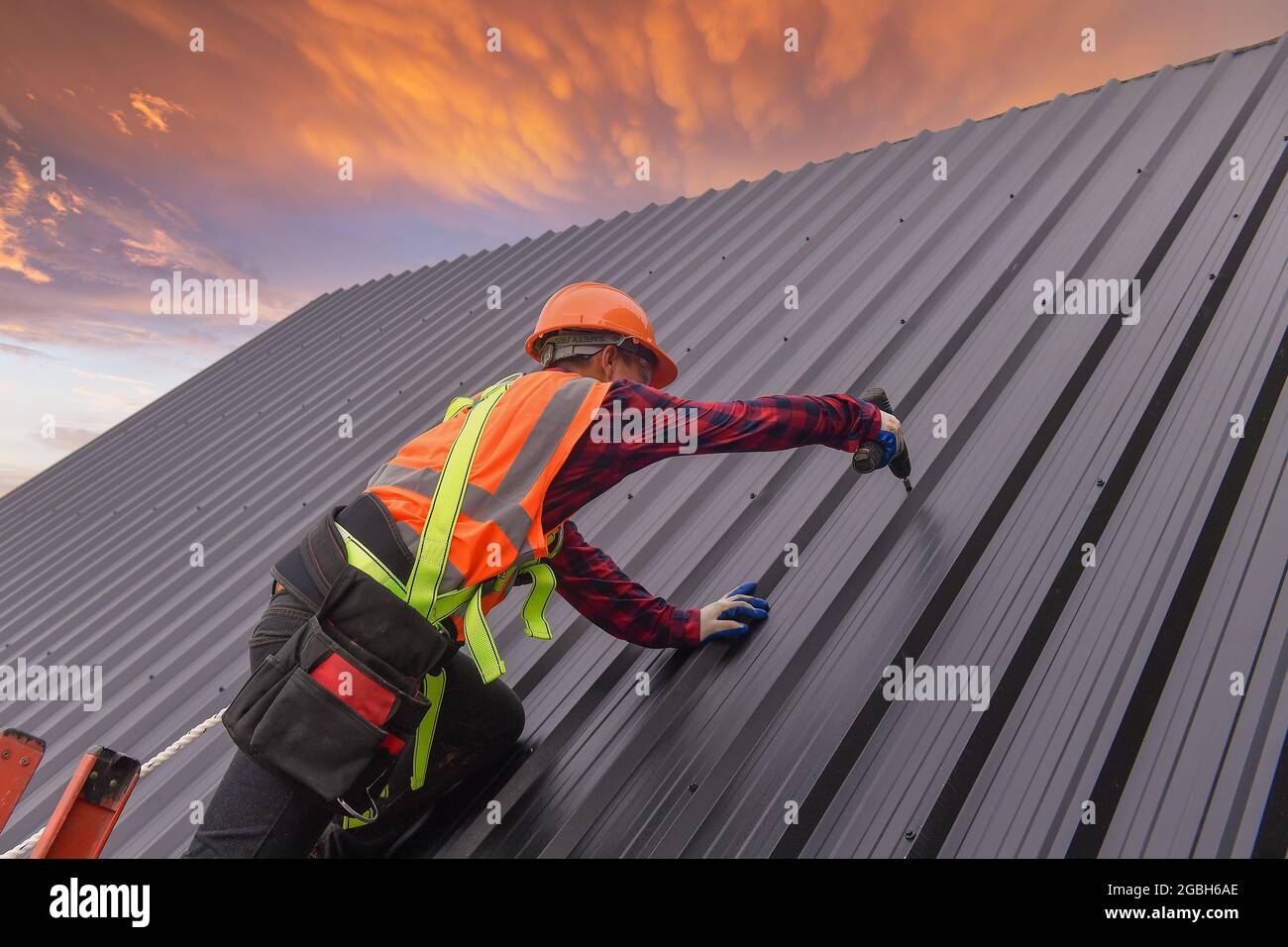 Construction worker installing metal sheets on a roof, Thailand Stock Photo