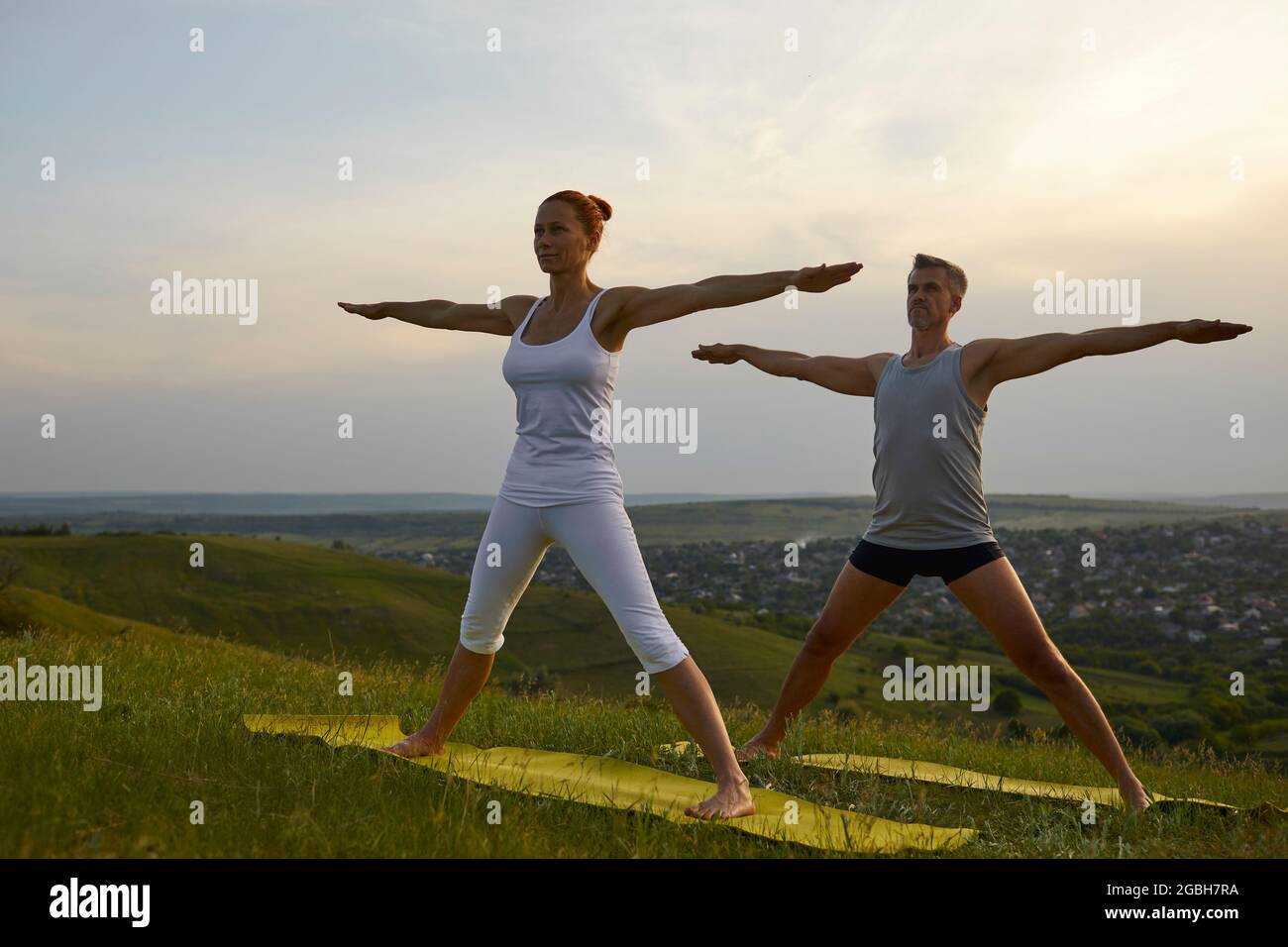 Middle aged man and woman doing Five Pointed Star practicing yoga on grassy hill in the morning Stock Photo