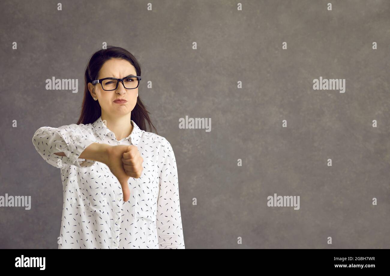 Frustrated woman with a negative expression expresses her displeasure by showing thumb down. Stock Photo
