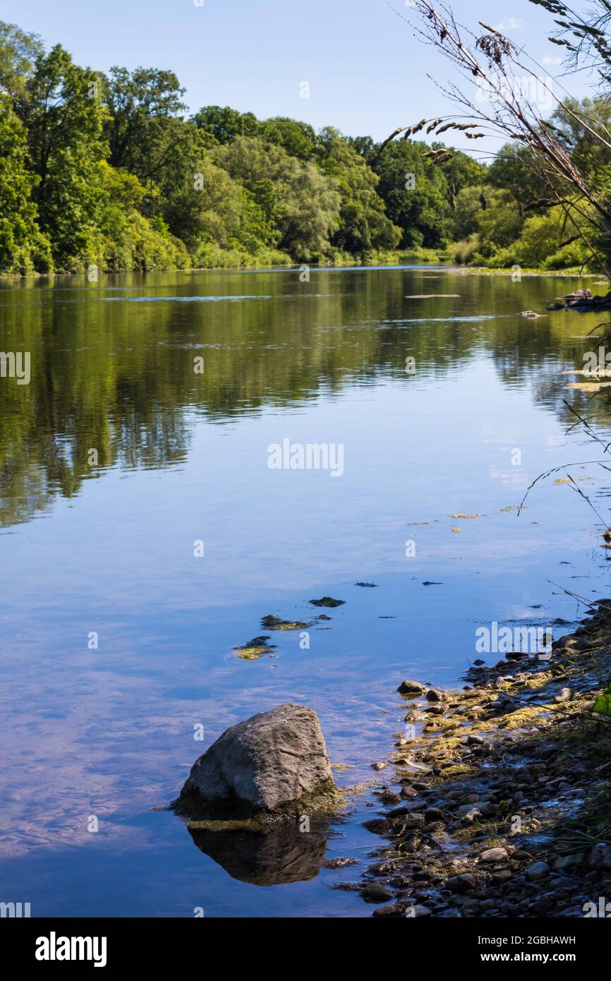 Vertical of Thames River in Ontario, Canada. Reflection of trees in background, rock in foreground. Stock Photo