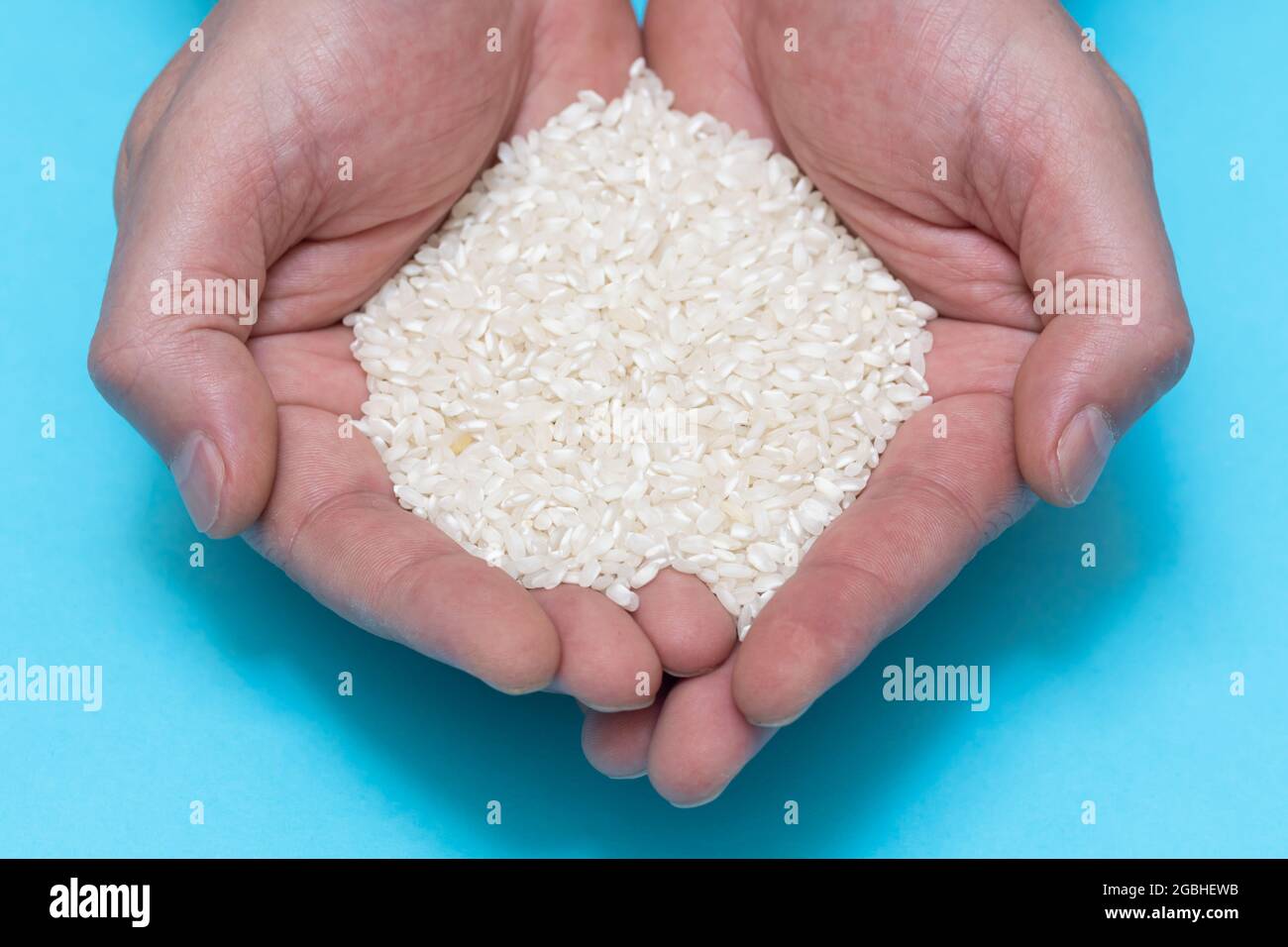 A person's hands holding a handful of rice on blue background. food