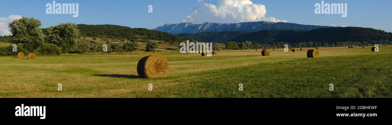 Hay bales over the rural fields at Rocca di Mezzo upland , with high mountains on the background , Abruzzo , Italy Stock Photo