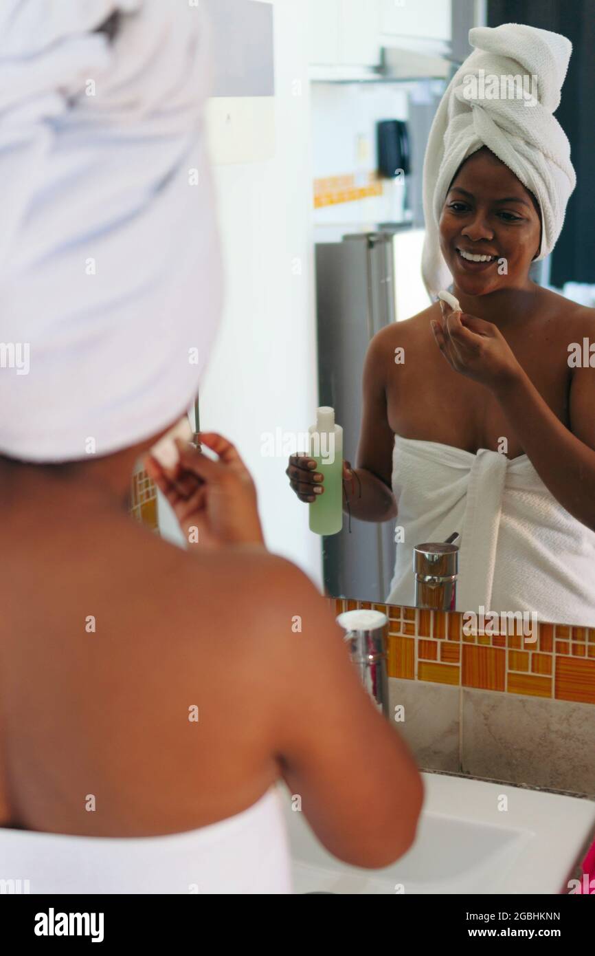 African woman cleans her face in the morning, standing in front of a mirror. Stock Photo