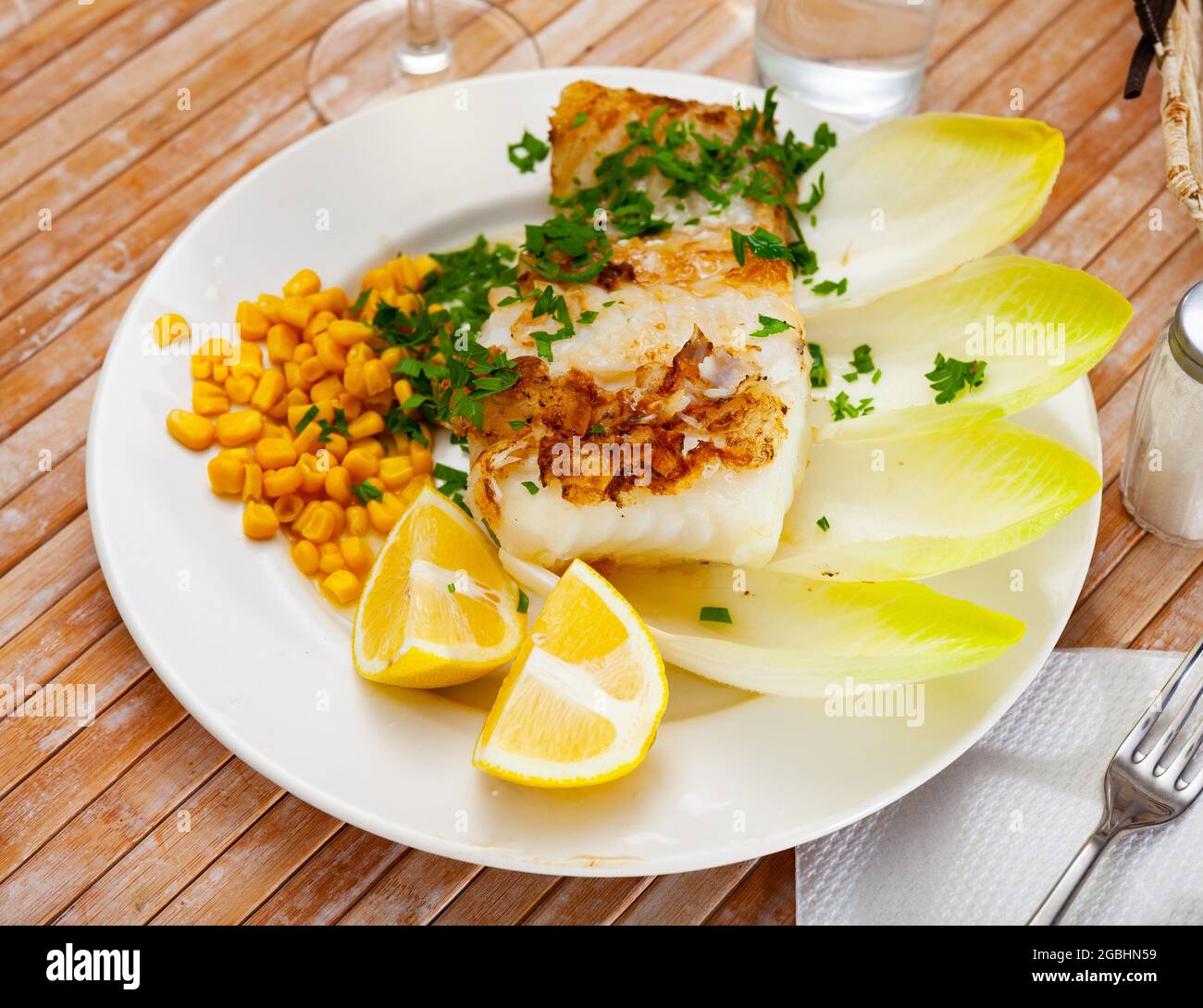 Fried rockling fillet with corn, lemon and greens Stock Photo