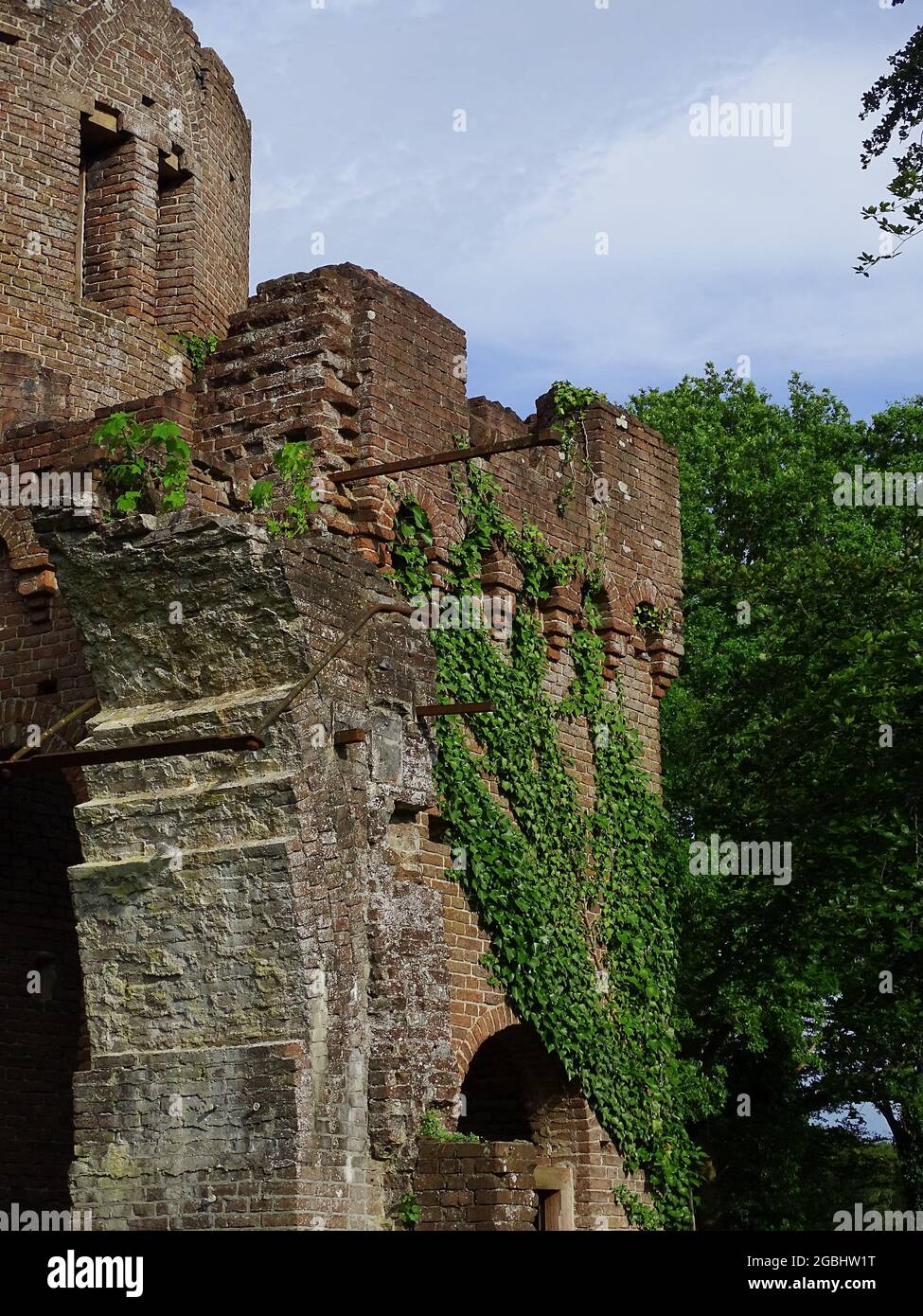 A folly (fake ruin) with an ivy against the old walls, grass in the foreground and a blue sky with clouds Stock Photo