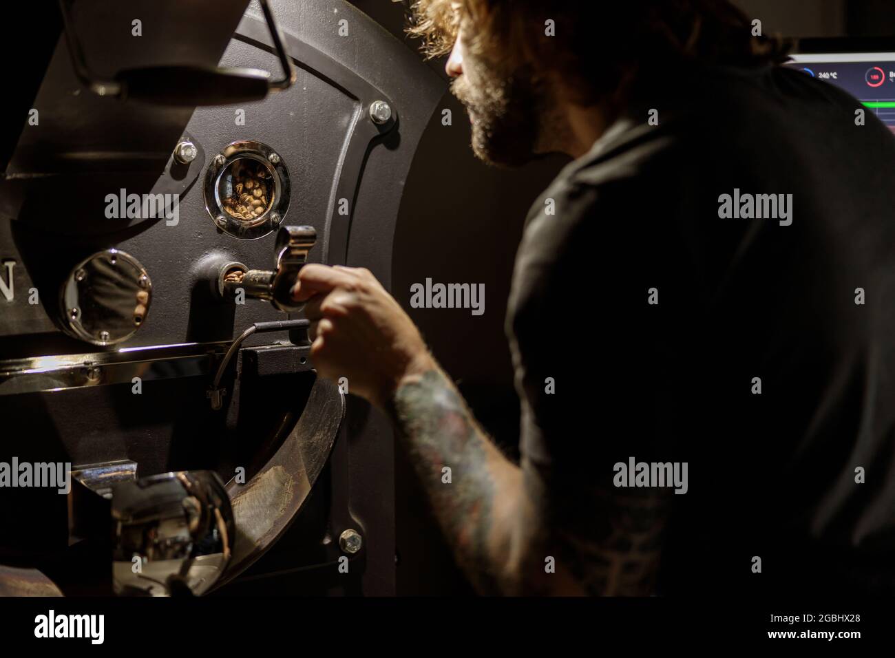 Bearded man using coffee roasting machine at factory Stock Photo