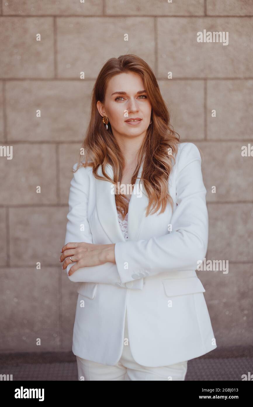 Business woman in white suit posing with crossing arms. Confident stylishly dressed woman Stock Photo