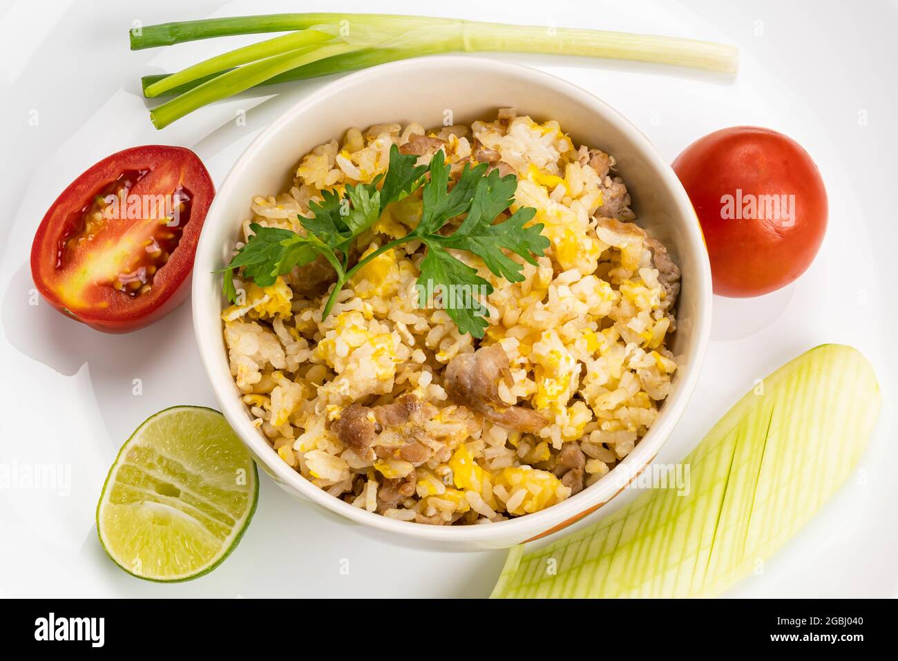 Top view of delicious homemade thai style pork and egg fried rice in ceramic bowl on white ceramic plate with whole and half tomato, sliced cucumber, Stock Photo