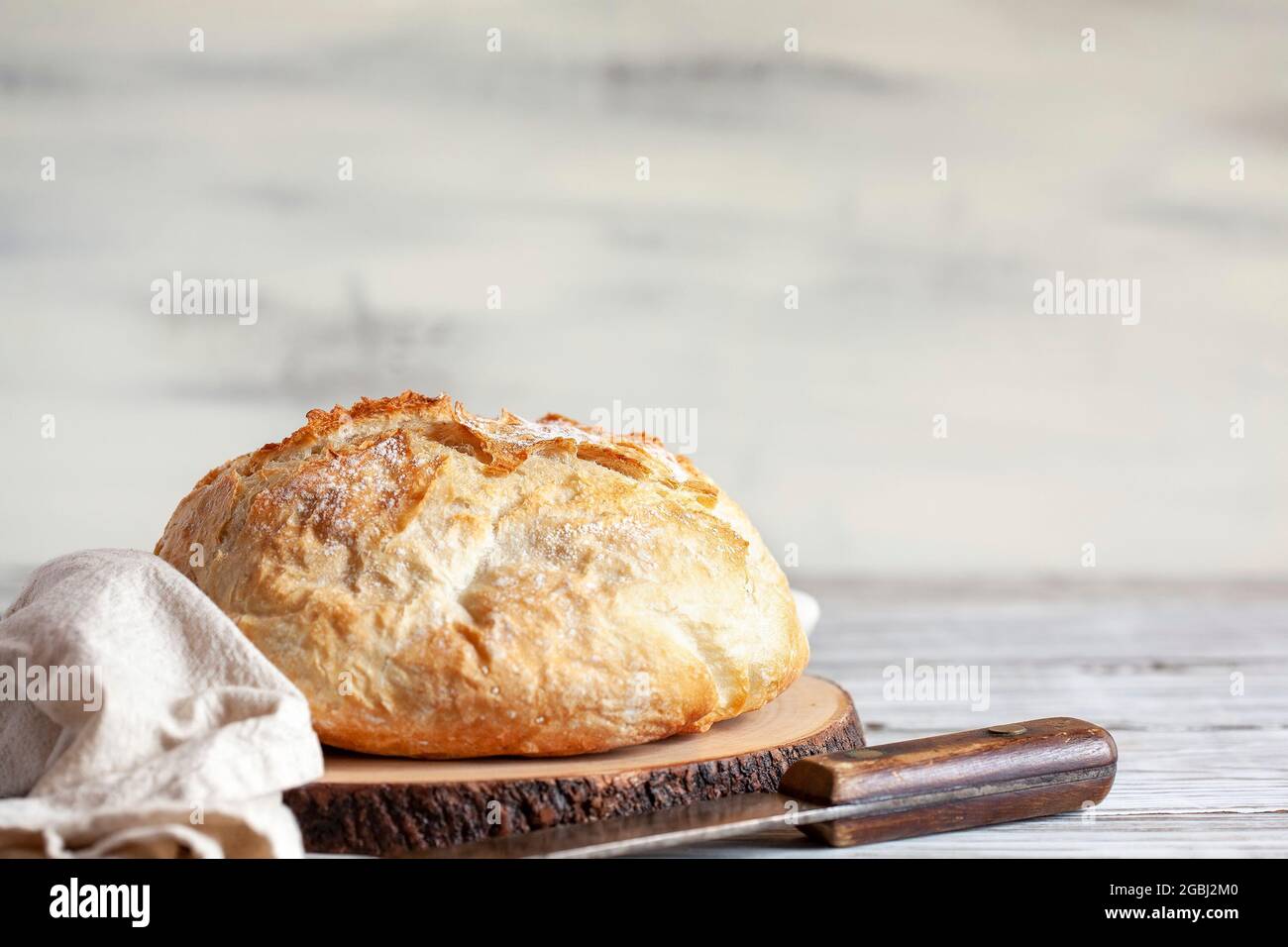 Fresh homemade artisan bread on a cutting board with tea towel and knife. Stock Photo