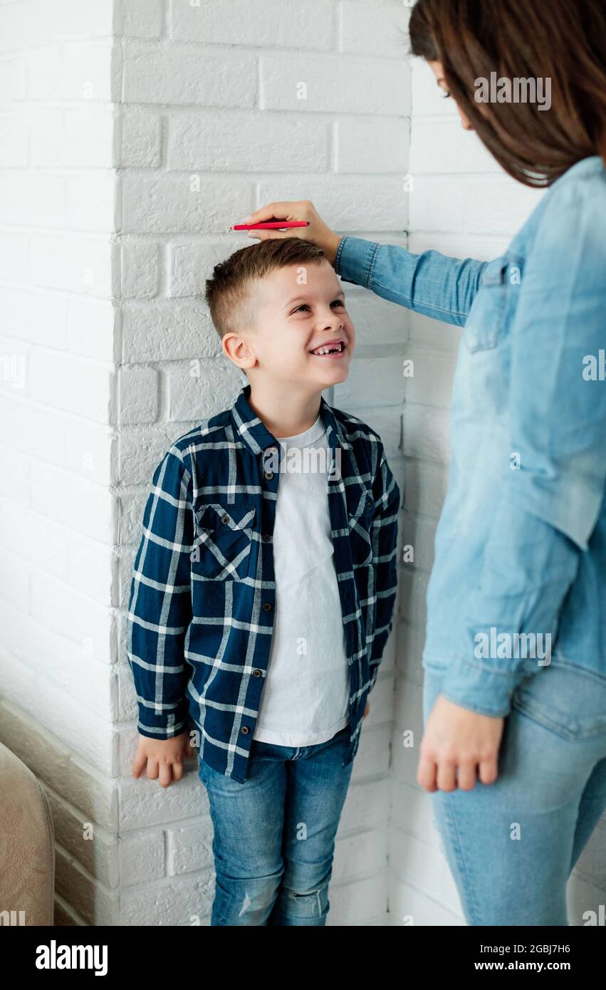 son mother measuring height growth childhood tall child heigth kid wall cute happy boy measure parent growth Stock Photo