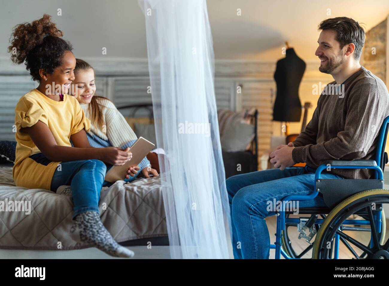 Happy father with disability in wheelchair enjoying time with children at home Stock Photo