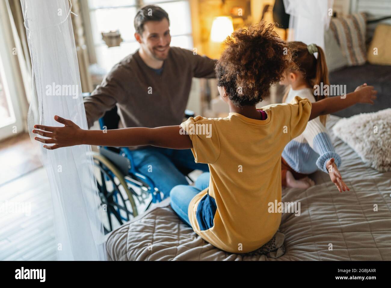 Portrait of happy loving father with disability in wheelchair hugging with multiethnic children Stock Photo