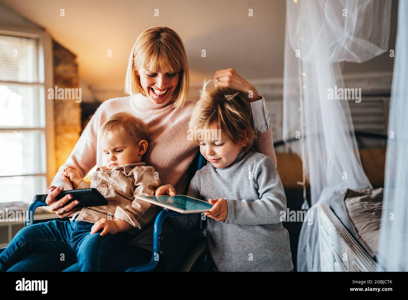 Happy smiling mother with disability in wheelchair playing with children at home Stock Photo