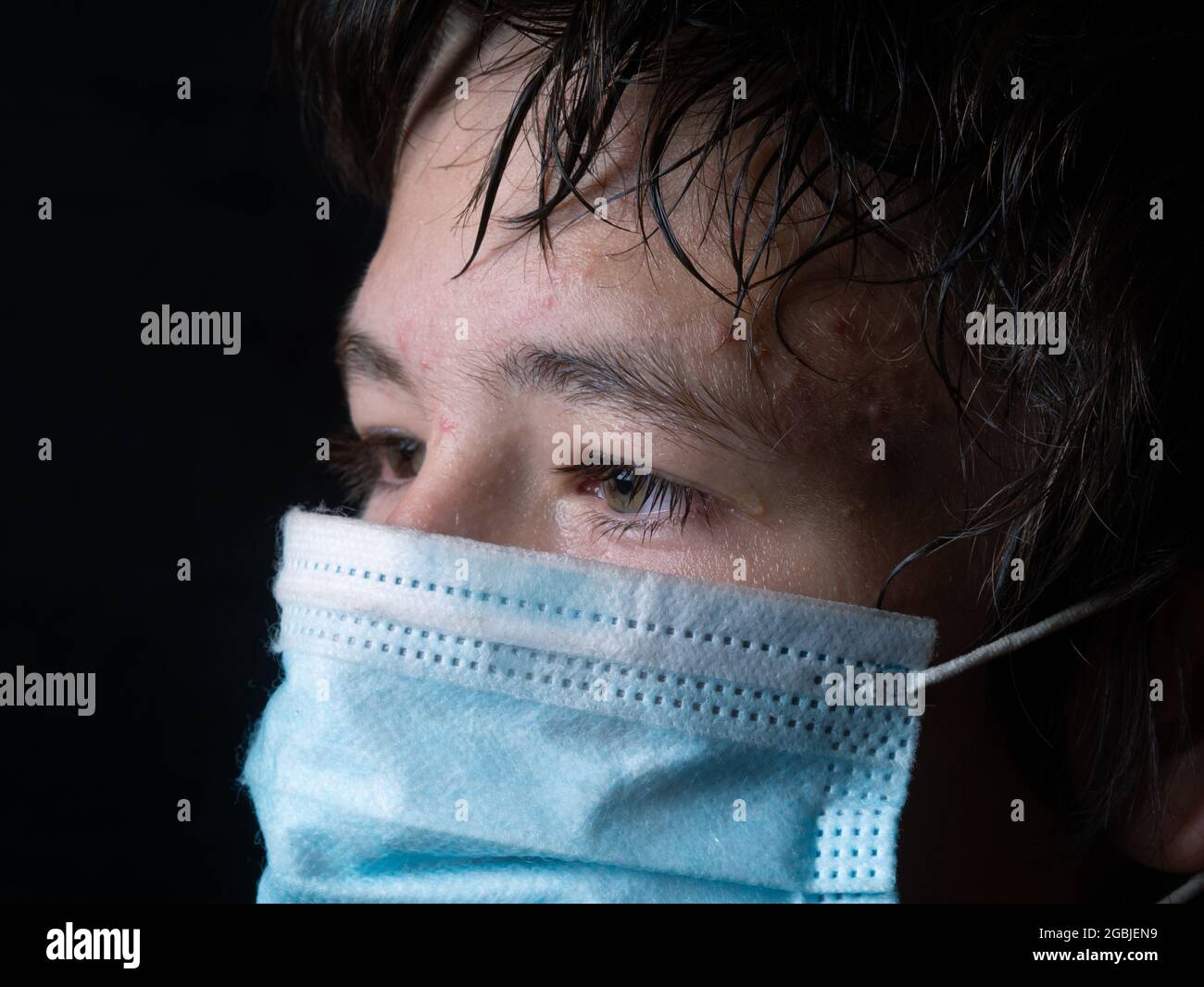 Crying Teenager With Medical Face Mask And Tears In Eyes Against Dark