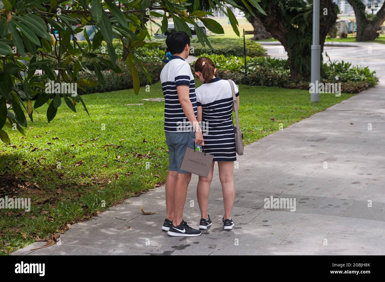 10.02.2018, Singapore, Republic of Singapore, Asia - A young couple wearing fashionable matching clothes is seen standing in a park in the city centre. Stock Photo