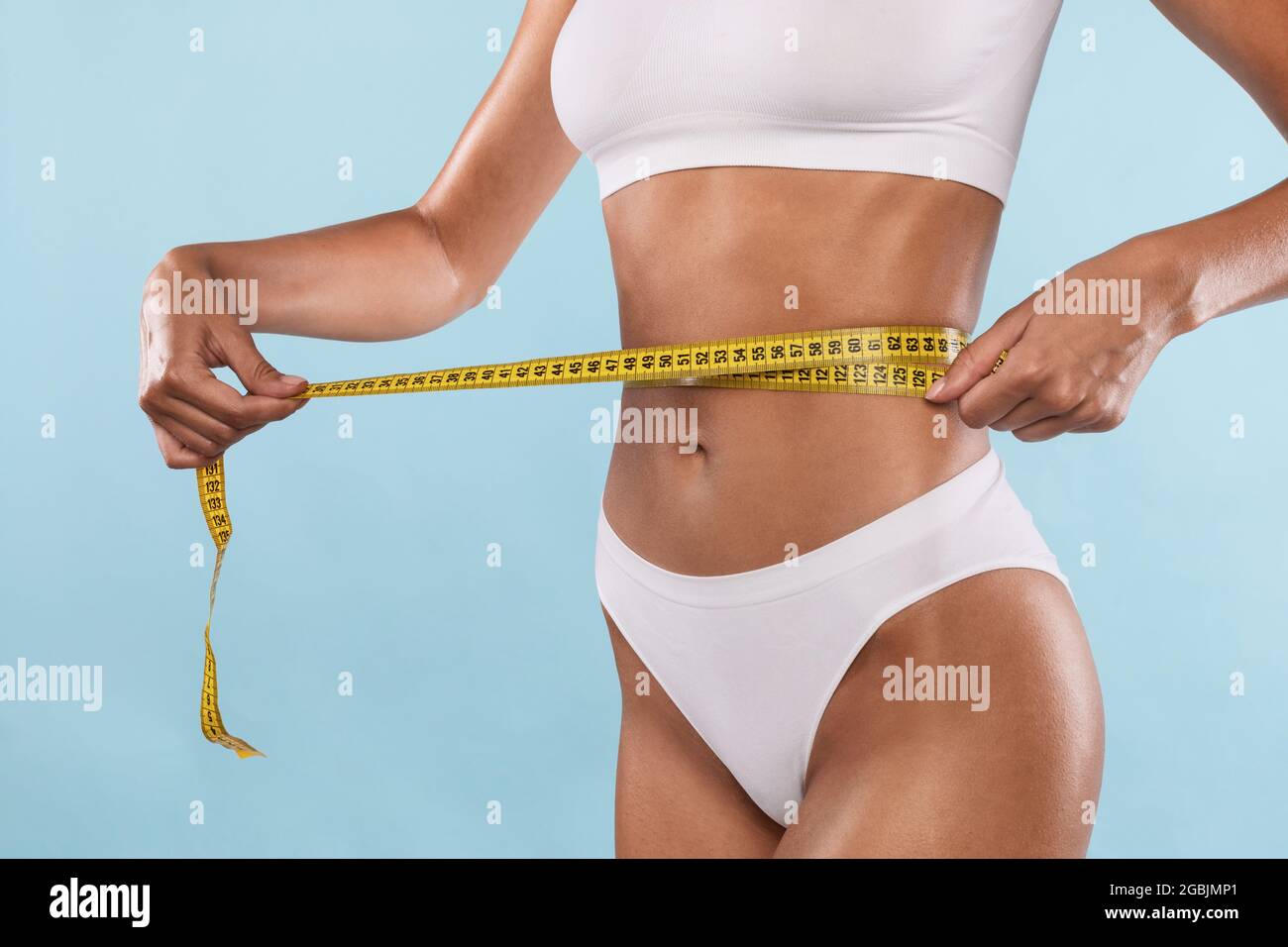 Slim young woman measuring her thin waist with a tape measure, close up  Stock Photo
