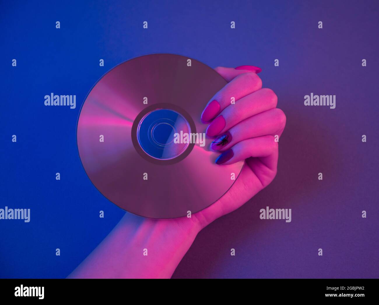 Compact disc in purple neon light and female hand with retrowave manicure. Stock Photo