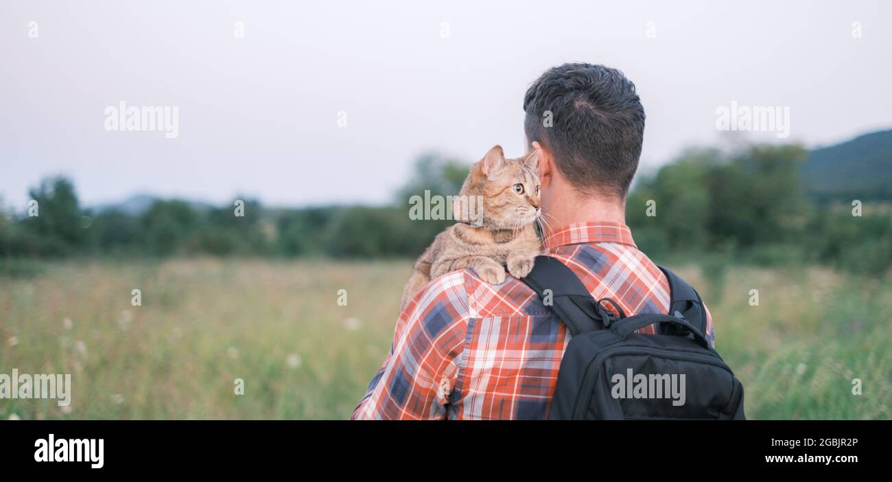 Cat sitting on shoulder of man in summer park. Stock Photo