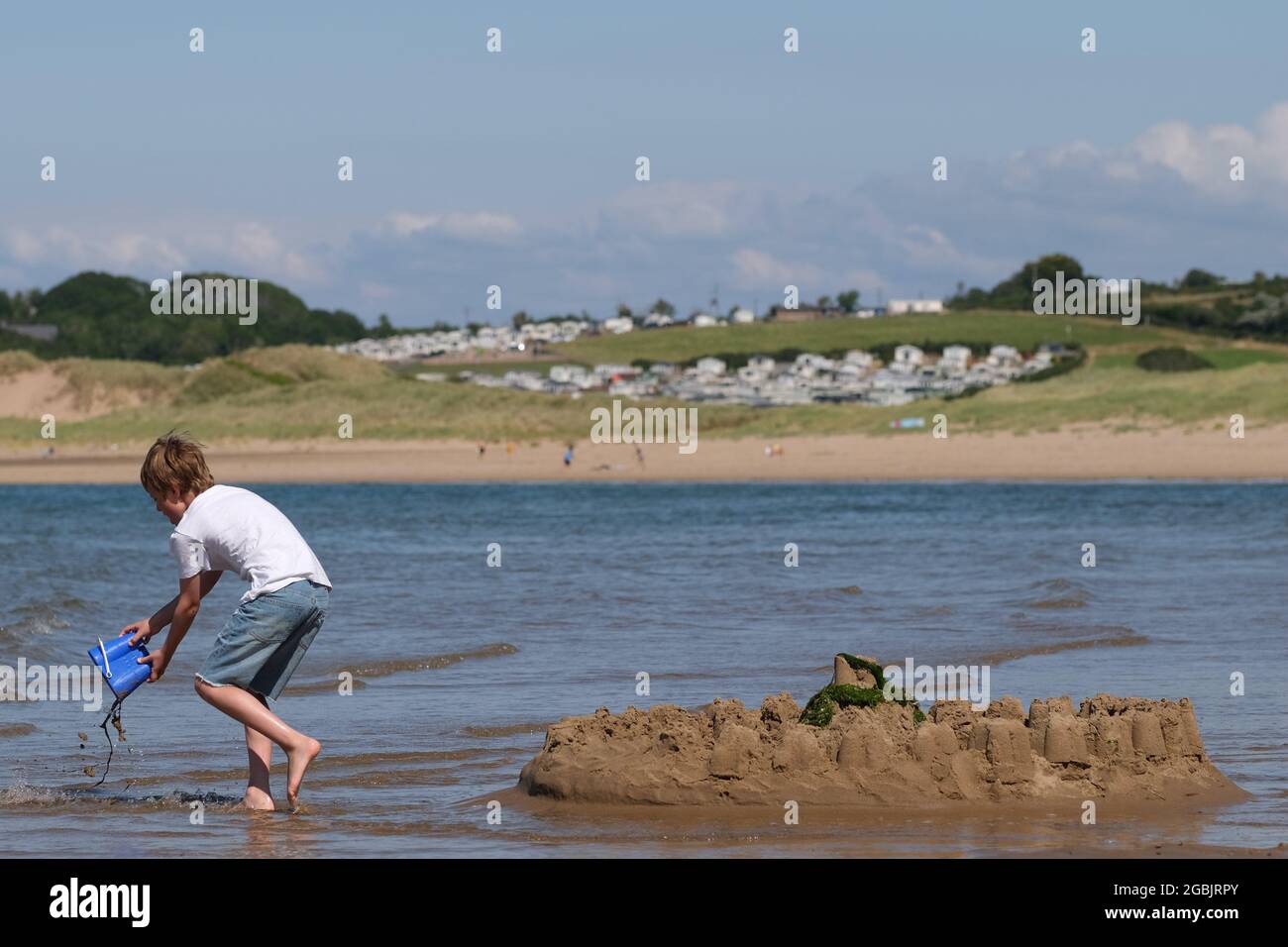 Gower, Swansea, UK. 4th August, 2021.  UK weather: sunny and warm with a light southerly breeze at Broughton beach on the Gower peninsula, as the forecast pedicts wet and  changeable weather in the coming days. A young boy battles to save his sand castle against the incoming tide. Credit: Gareth Llewelyn/Alamy Live News Stock Photo