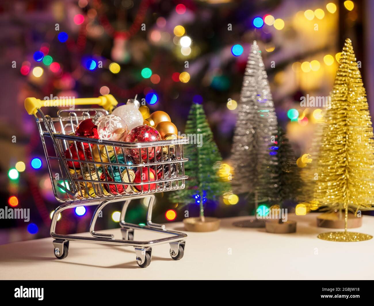 small shopping cart full of christmas decorations and with lights on a festive christmas tree background Stock Photo