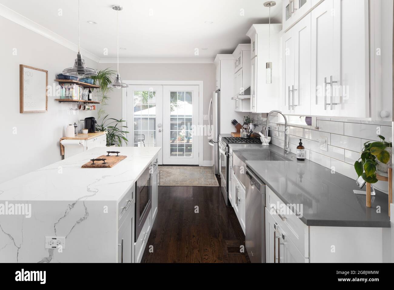 A white renovated kitchen with a waterfall granite island, stainless steel Whirlpool appliances, and hardwood floors. Stock Photo