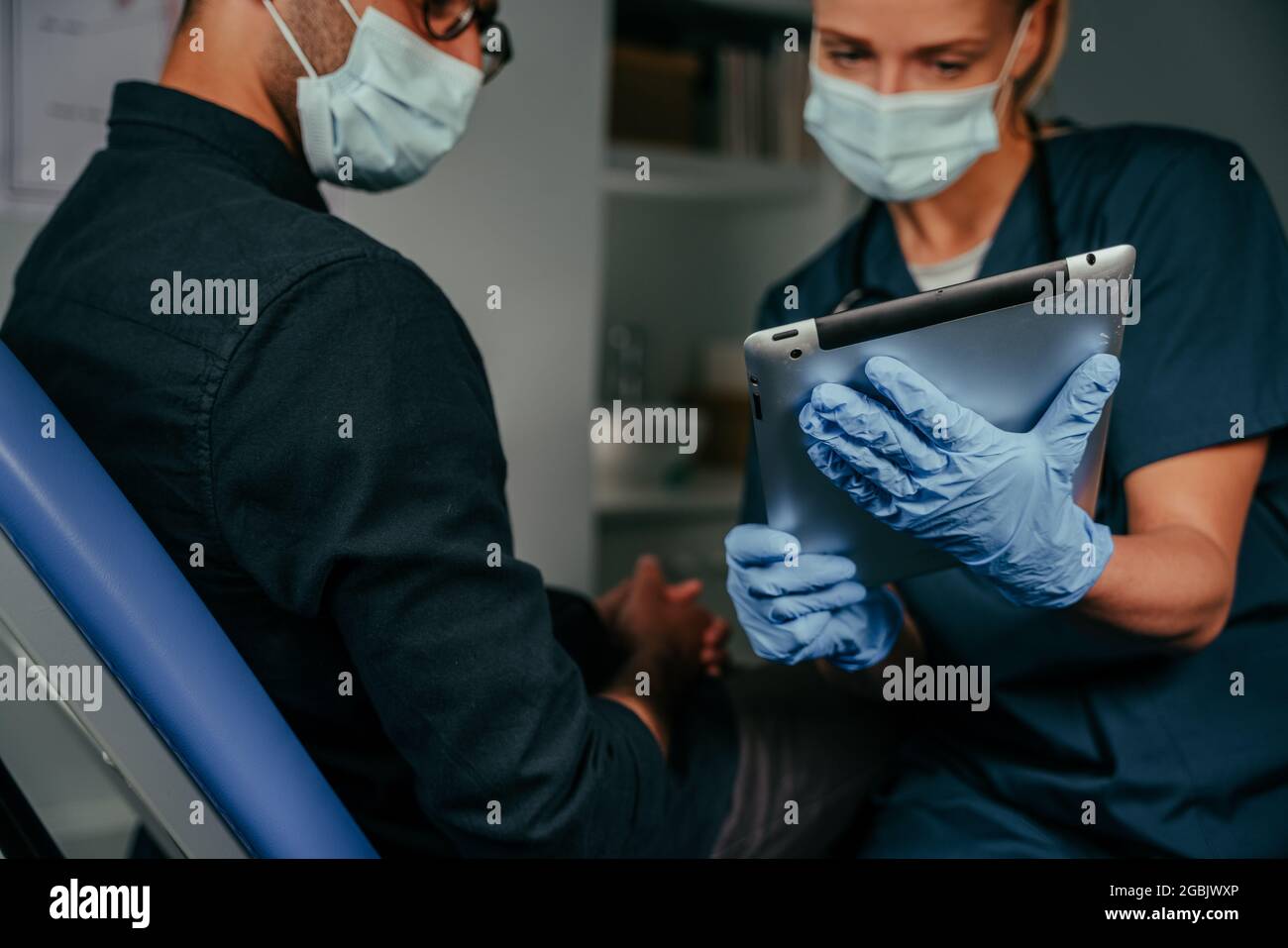 Mixed race male patient chatting to female nurse holding digital tablet Stock Photo