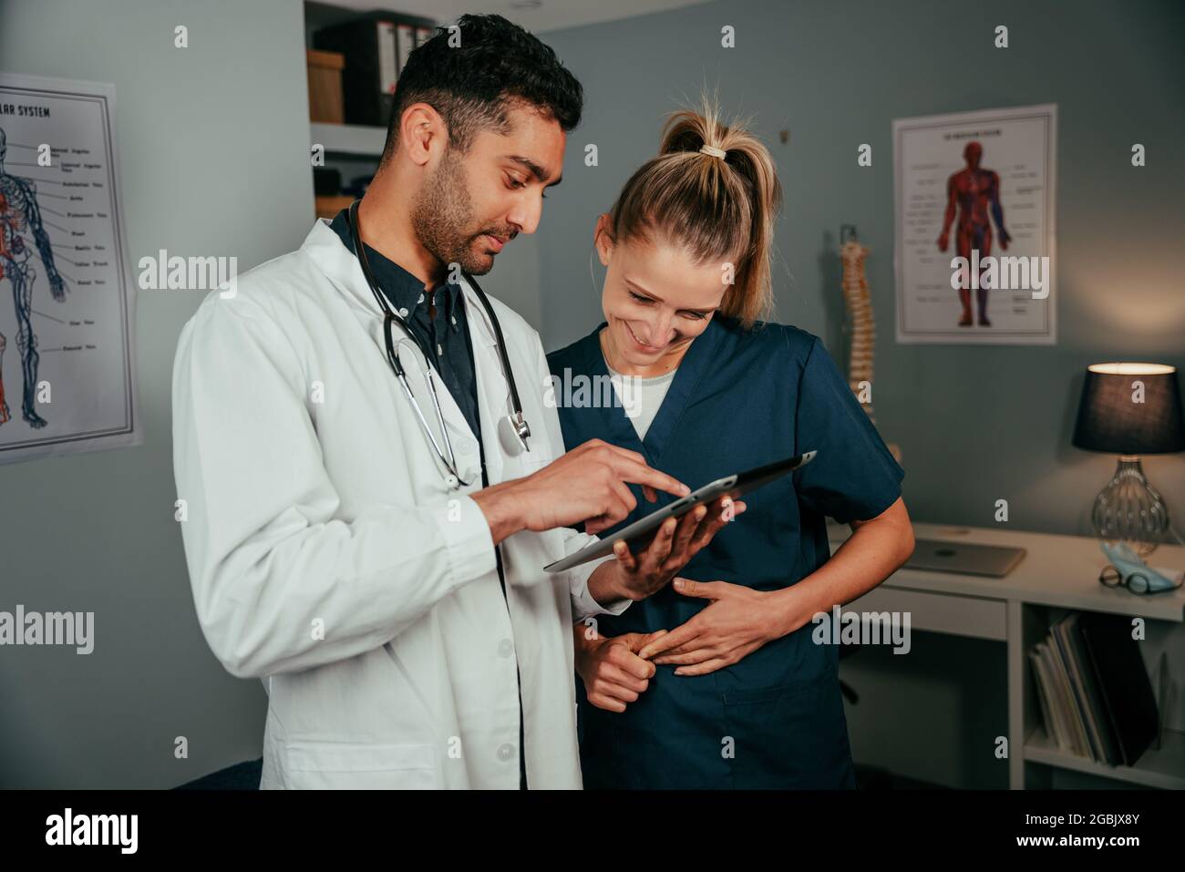 Mixed race couple of nurses talking about schedule while reading on digital tablet  Stock Photo