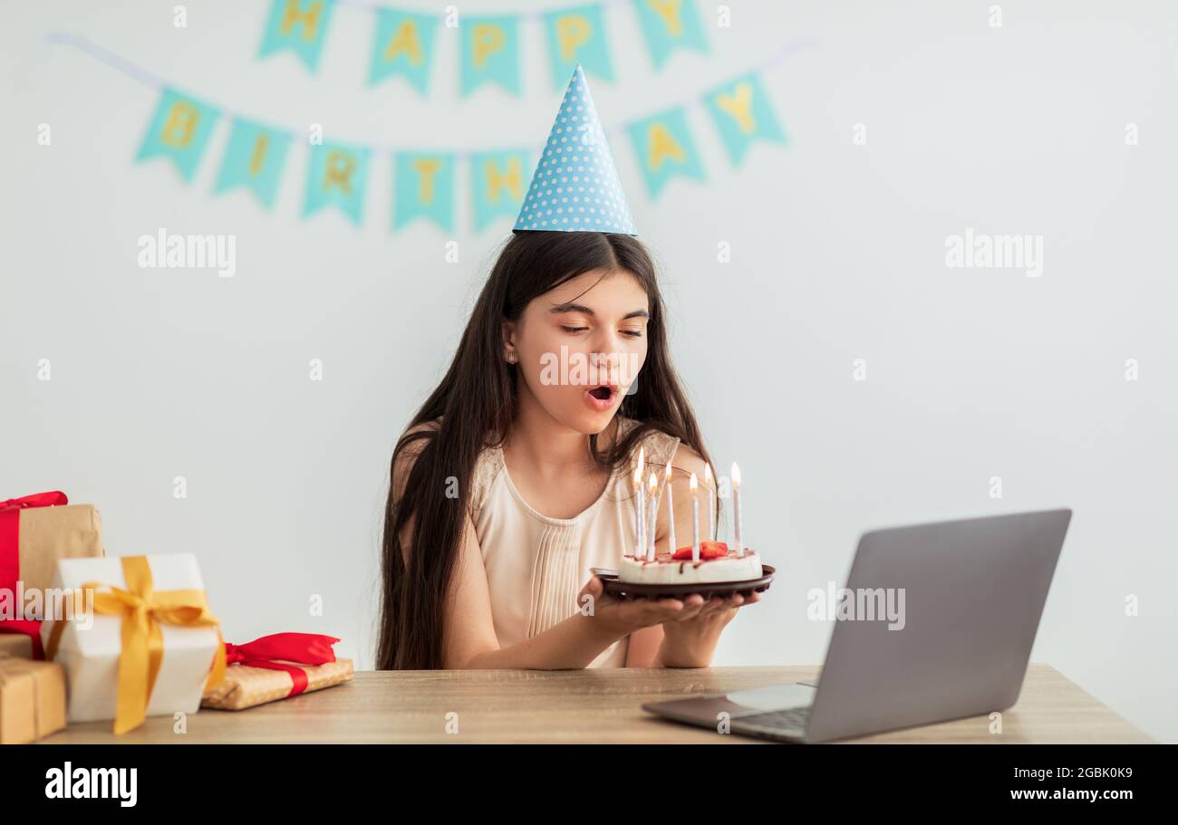 Indian teenage girl in festive hat having online birthday party, blowing  candles on cake in front of laptop webcam Stock Photo - Alamy