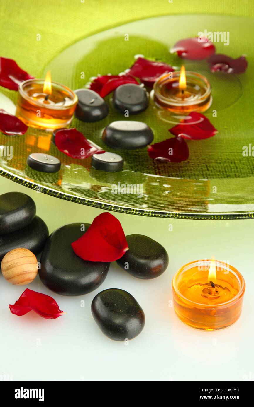 spa stones with rose petals and candles in water on plate, isolated on ...