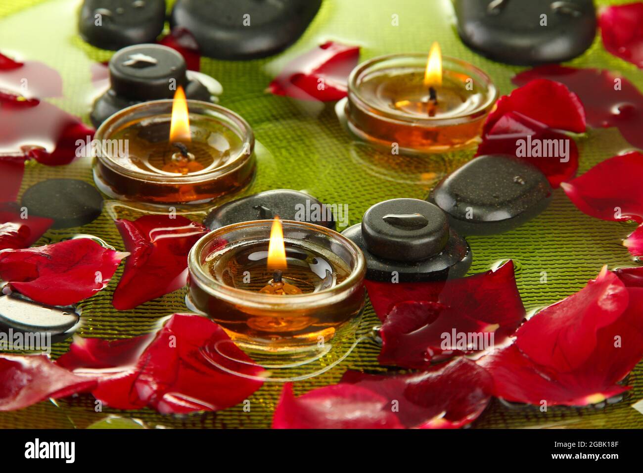 spa stones with rose petals and candles in water on plate Stock Photo ...