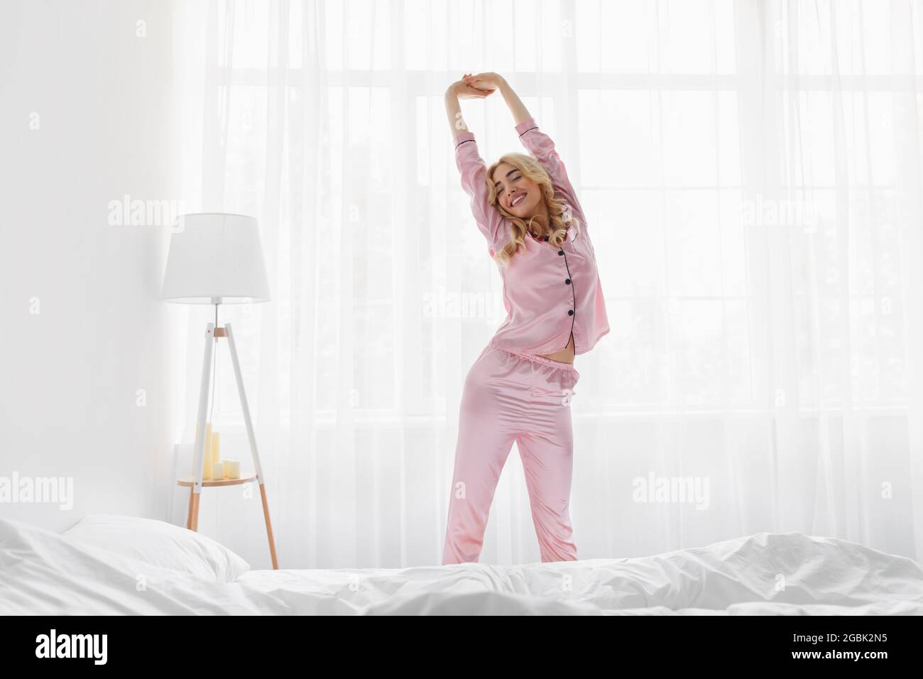 Wake up in morning, happy young lady greets new day with warm sunlight flare Stock Photo