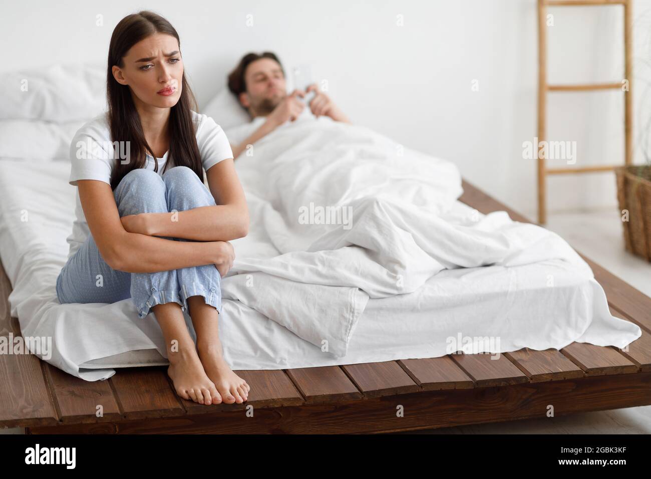 Unhappy Girlfriend Sitting While Cheating Husband Texting On Phone Indoor Stock Photo