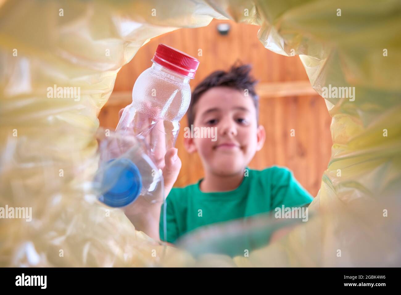 image from inside a recycling bin with a yellow bag of a child throwing a plastic bottle to recycle in which the child's face is out of focus Stock Photo