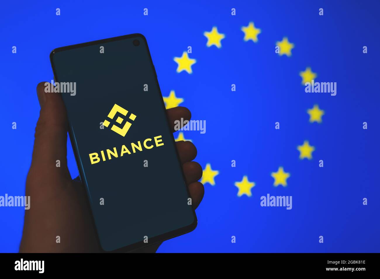 Binance app logo on smartphone in hand with the blurred European Union flag background. Binance in Europe, EU regulations news. Crypto exchange Stock Photo