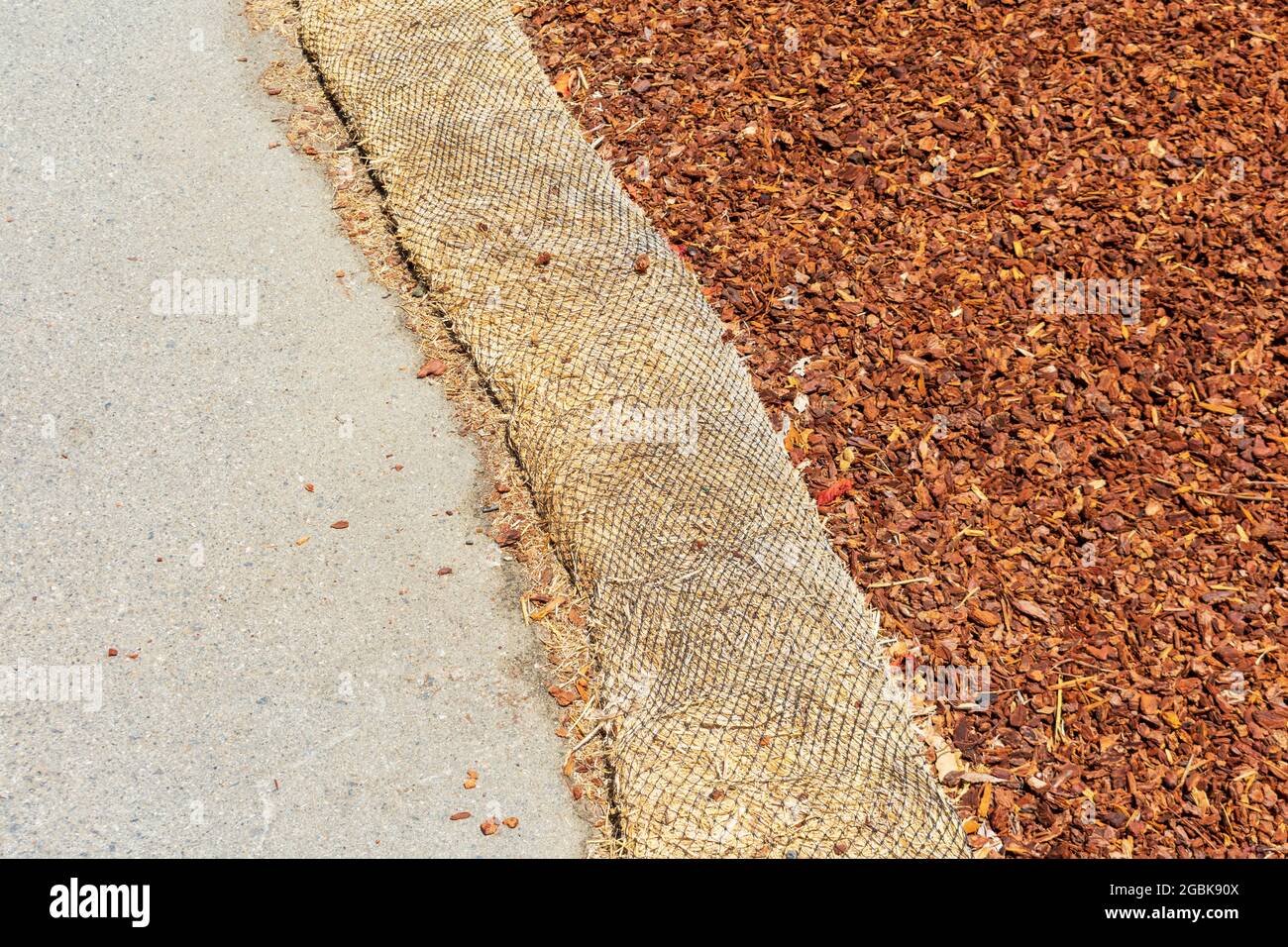 Straw wattle separate ground covered with mulch and asphalt walkway to reduce debris runoff during landscaping, construction and maintenance project. Stock Photo