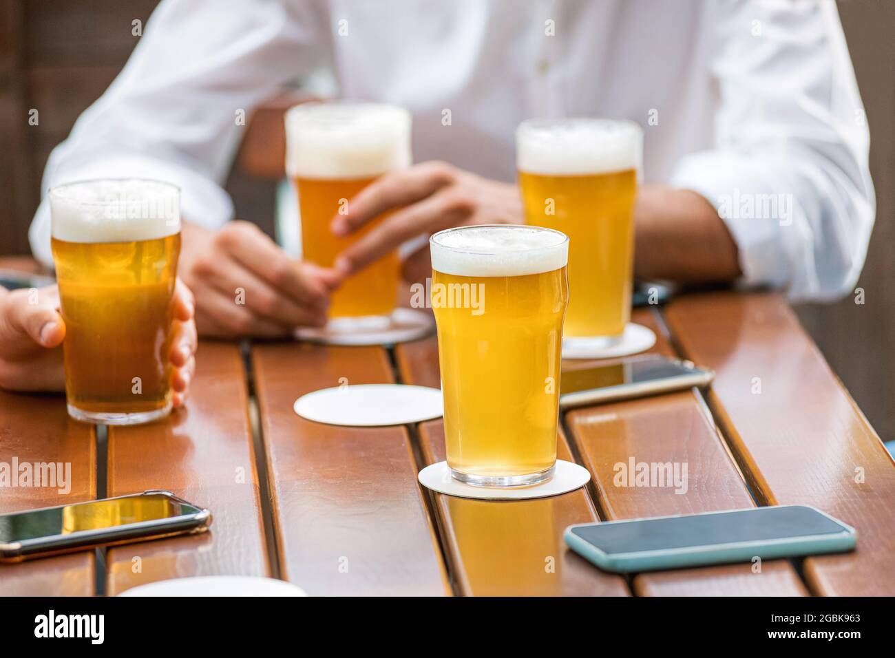 Glasses of ice cold beer with frothy heads on a pub table alongside the hands of a group of friends enjoying a relaxing meeting Stock Photo