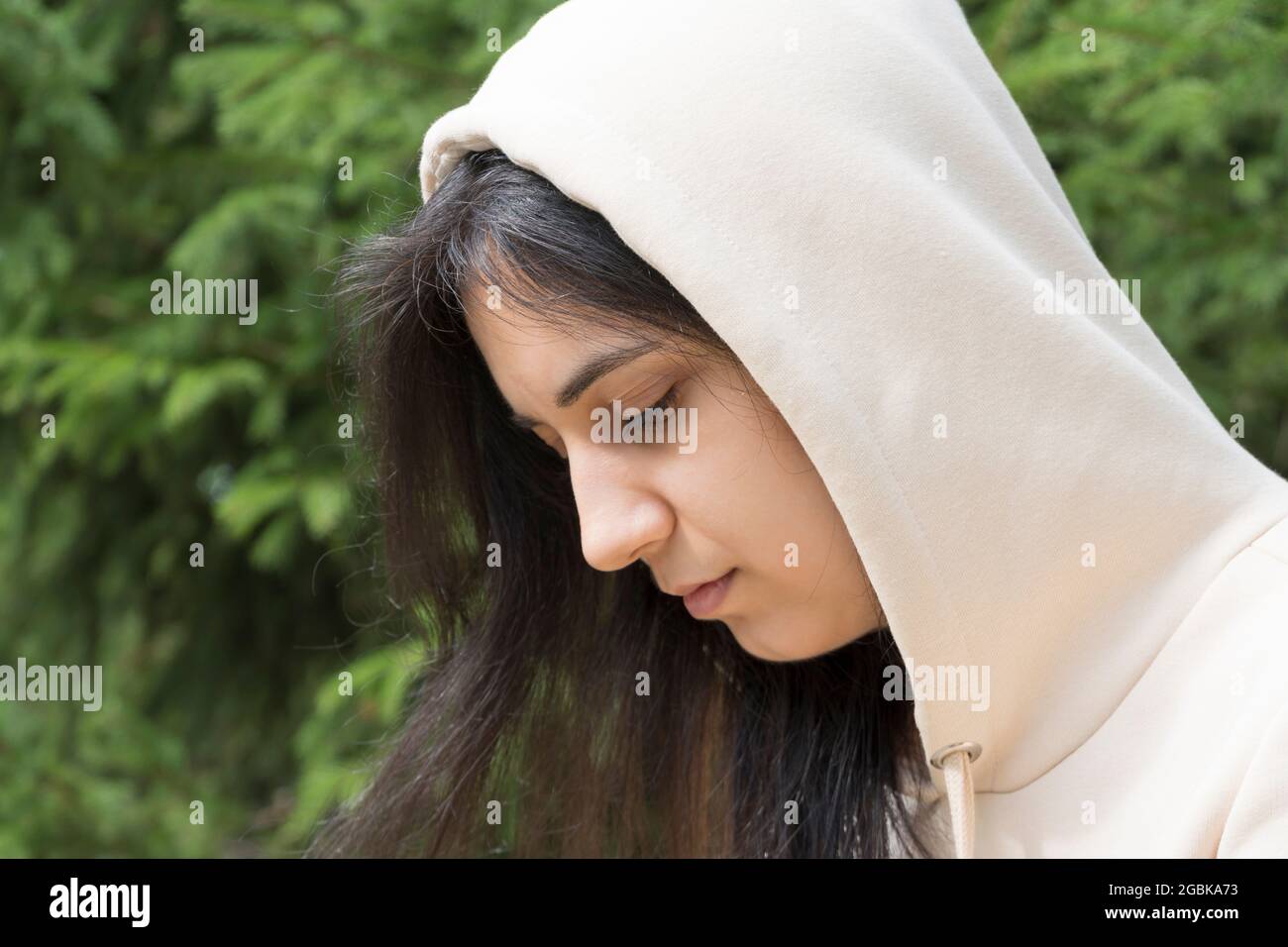 The hooded brunette looks down. The sad girl looked down. Close-up of a beautiful girl in depression. Melancholy, victim, bullying. Teen in casual out Stock Photo