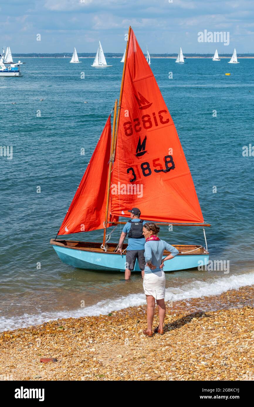 mirror dinghy being launched by young couple, mirror dinghy launch from beach, small sailing dinghy on beach, mirror siling dinghy with young couple. Stock Photo