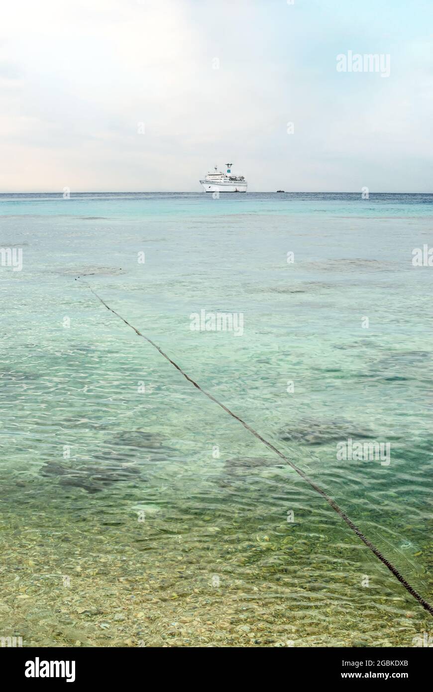 Distant view at the cruiseship Amadea moored in a lagoon off Tuamotu Island with a mooring rope leading to the ship Stock Photo