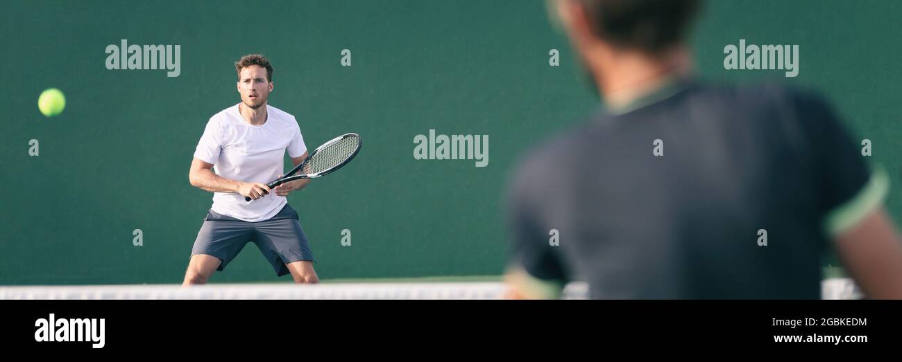Tennis players playing on green court man focused on other player hitting ball with racket panoramic. Men sport athletes playing tennis match. Two Stock Photo