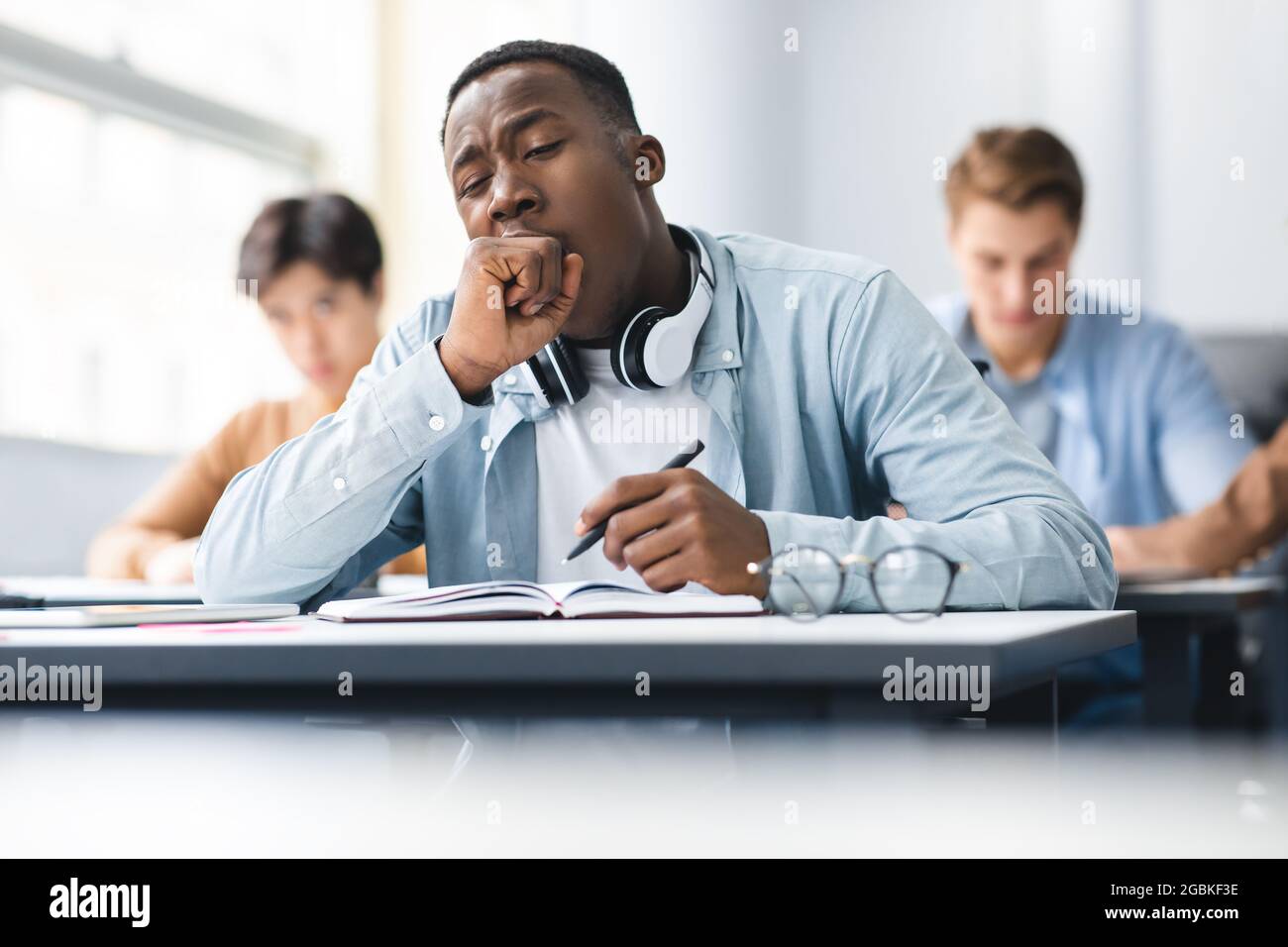Black male student yawning sitting at desk in class Stock Photo